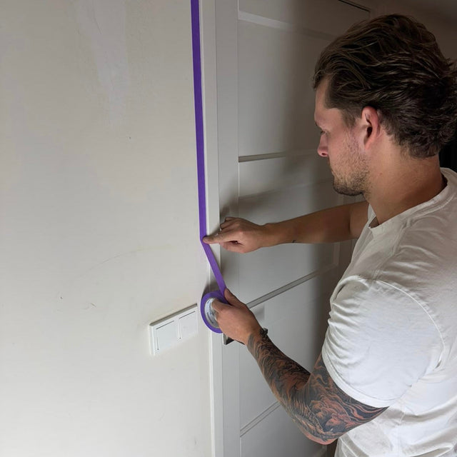 Schilder drukt de rand van paarse MOOZERS Washi tape aan langs een wit deurkozijn